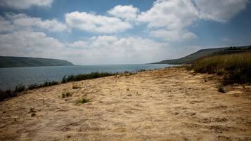 A sandy beach with a calm lake and distant hills under a partly cloudy sky.