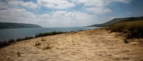 A sandy beach with a calm lake and distant hills under a partly cloudy sky.