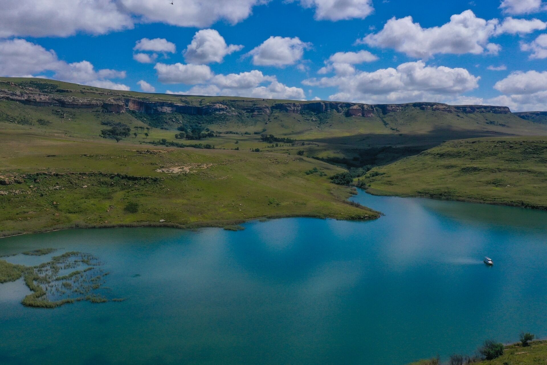 Una vista panoràmica d'una vall amb un llac, envoltada de turons verds i un cel serè.