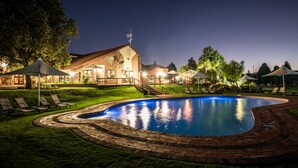A swimming pool with a brick border, surrounded by lounge chairs and a building with a sloped roof. - First Group Qwantani (Maluti a Phofung)
