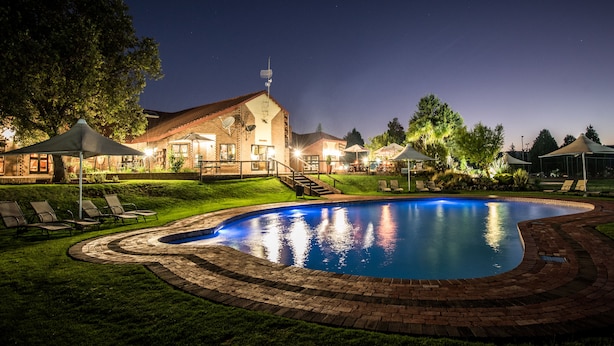 A swimming pool with a brick border, surrounded by lounge chairs and a building with a sloped roof. - First Group Qwantani (Maluti a Phofung)
