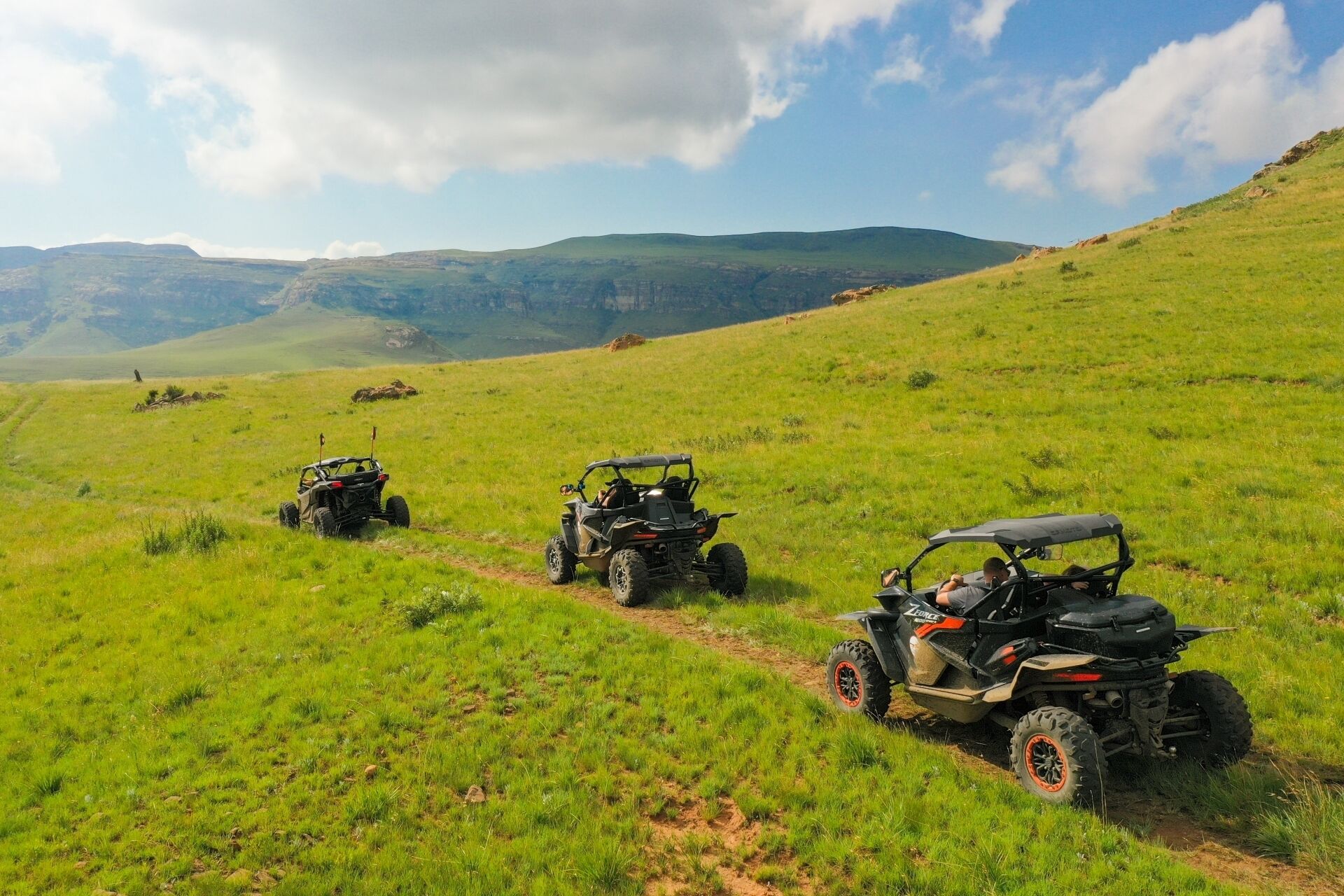 Three off-road vehicles parked on a grassy path in a hilly landscape.
