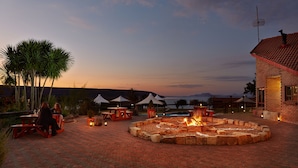 An outdoor patio area with a fire pit, picnic tables, and umbrellas. - First Group Qwantani (Maluti a Phofung)