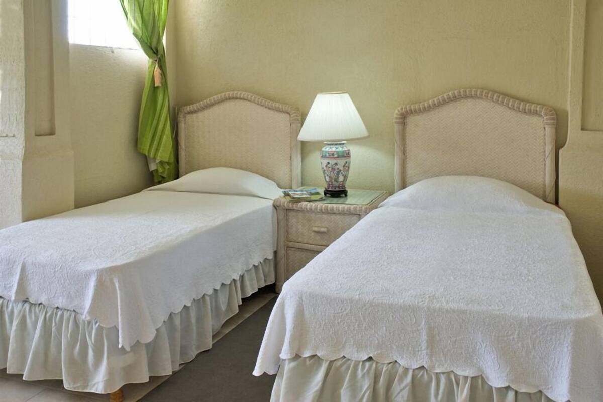 A room with two single beds, each with a white bedspread and a decorative lamp on a bedside table.