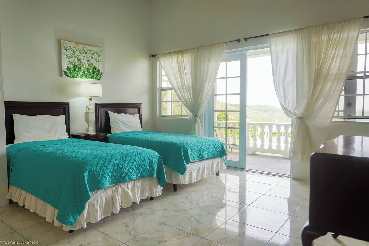A hotel room with two beds, a balcony, and a view of the outdoors.