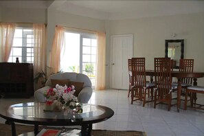 A living room with a sofa, a round coffee table with flowers, a dining table with chairs, and a door.
