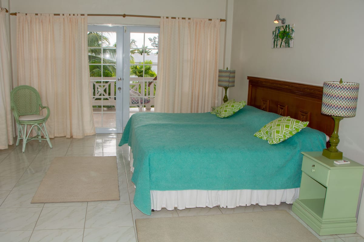 A bedroom with a bed, a chair, a nightstand, a lamp, and a view of the outdoors through a door.