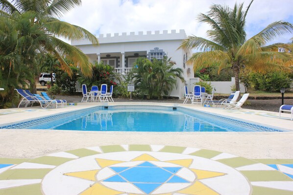 A pool area with lounge chairs, palm trees, and a building with a white facade.