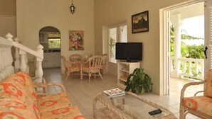 A living room with a sofa, a coffee table, a TV, and a balcony with a view. - Castles in Paradise (Vieux Fort)