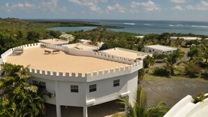 A white building with a flat roof, surrounded by greenery and a view of the ocean. - Castles in Paradise (Vieux Fort)