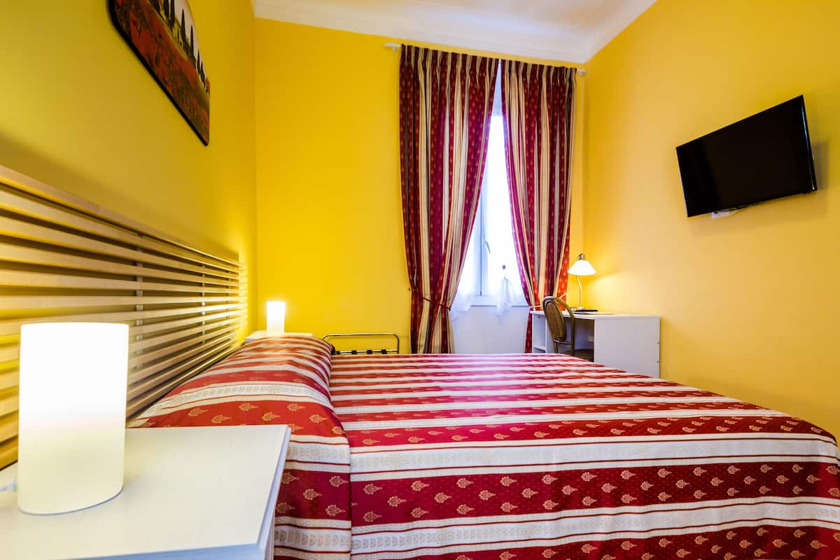 A hotel room with a bed, bedside table, lamp, curtains, and a TV on the wall.