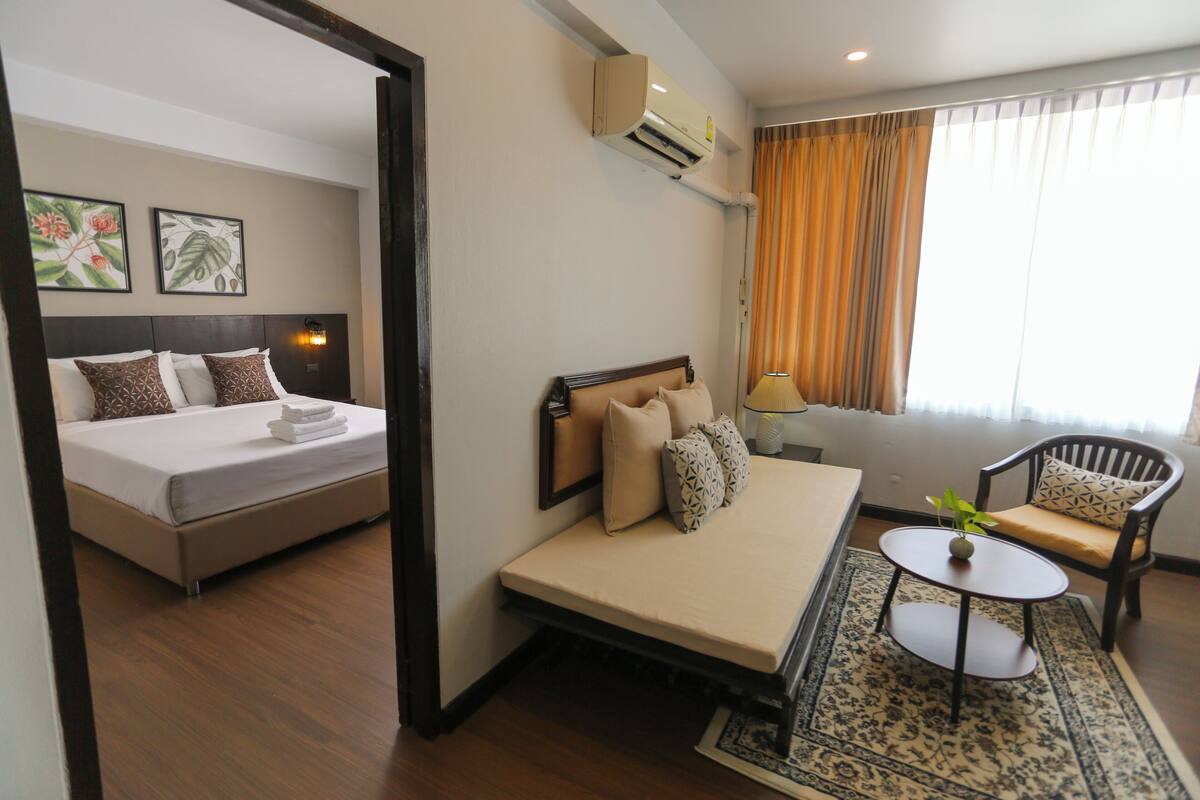 A hotel room with a bed, a sofa, a small table, and a window with curtains.