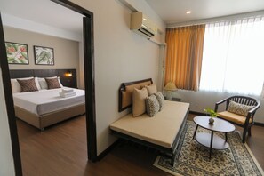 A hotel room with a bed, a sofa, a small table, and a window with curtains. - YMCA International Hotel (Chiang Mai)