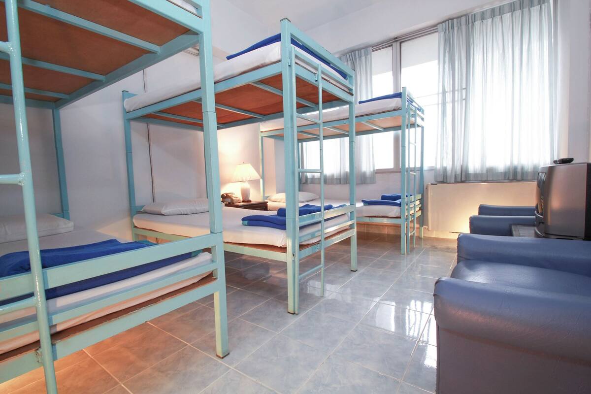 A dormitory room with bunk beds, a desk, a chair, and a television.