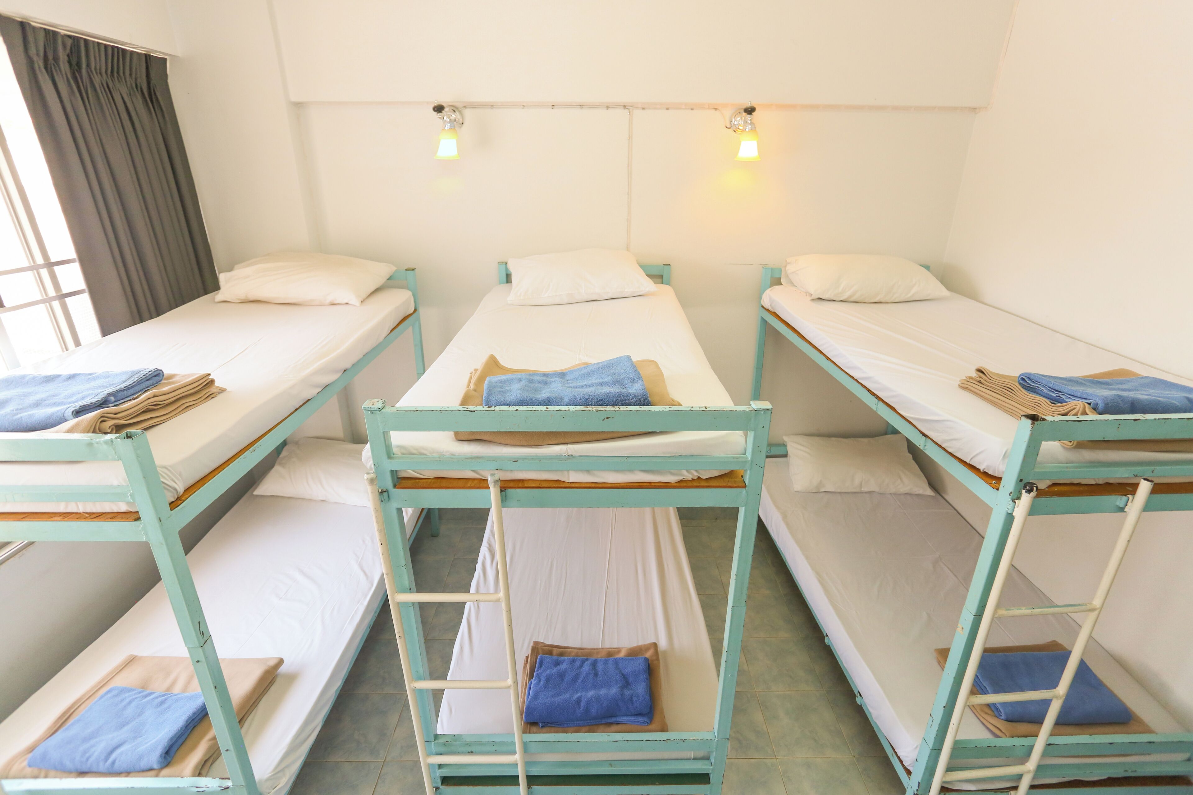 Ein Schlafsaalzimmer mit Etagenbetten, einer Stehleiter und einem Fenster mit Vorhängen.