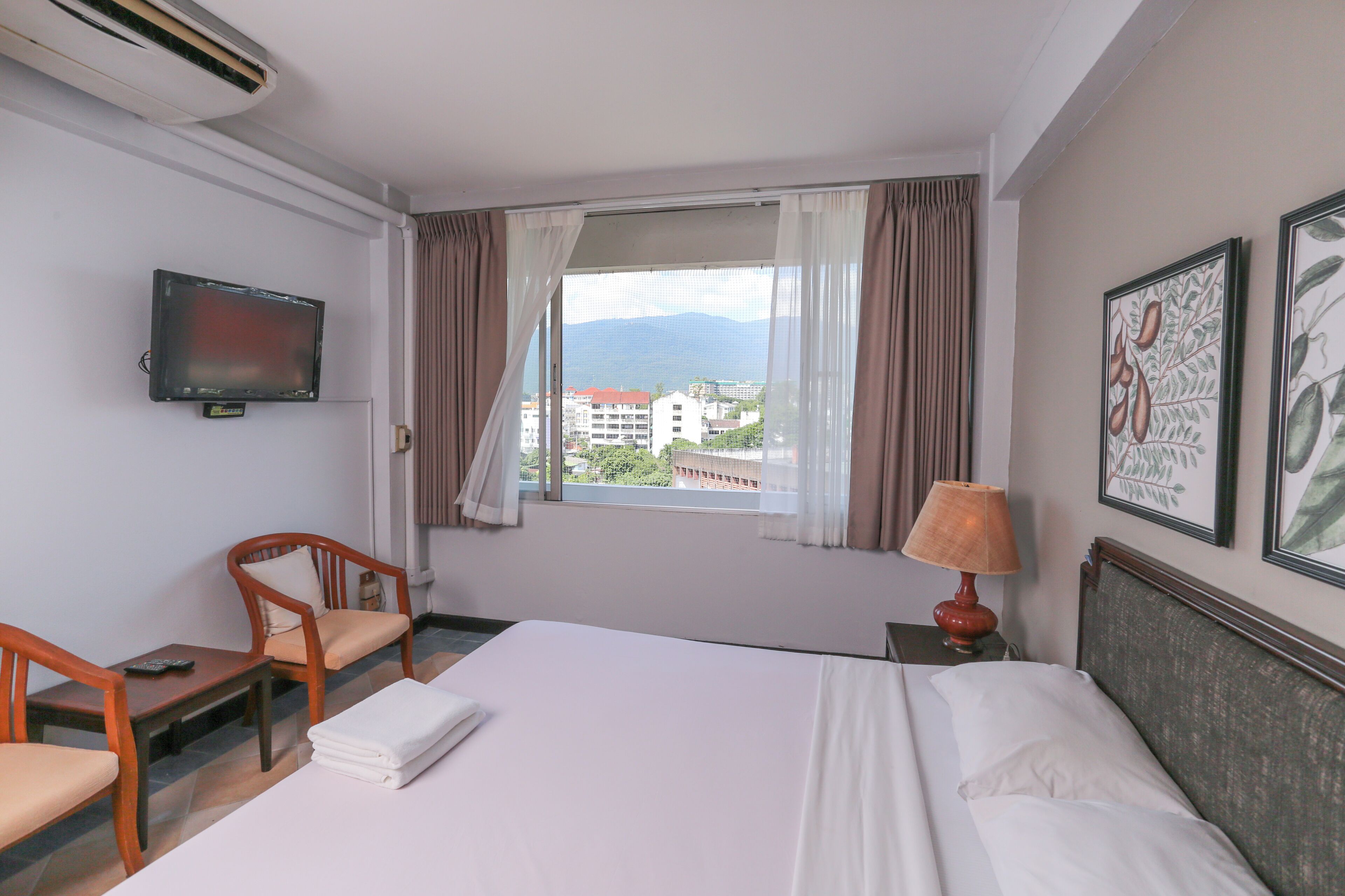 Een hotelkamer met een bed, een televisie, een raam met gordijnen, een stoel en een tafel.
