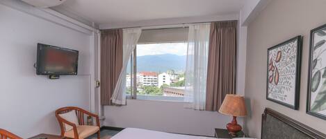 A hotel room with a bed, a television, a window with curtains, a chair, and a table.