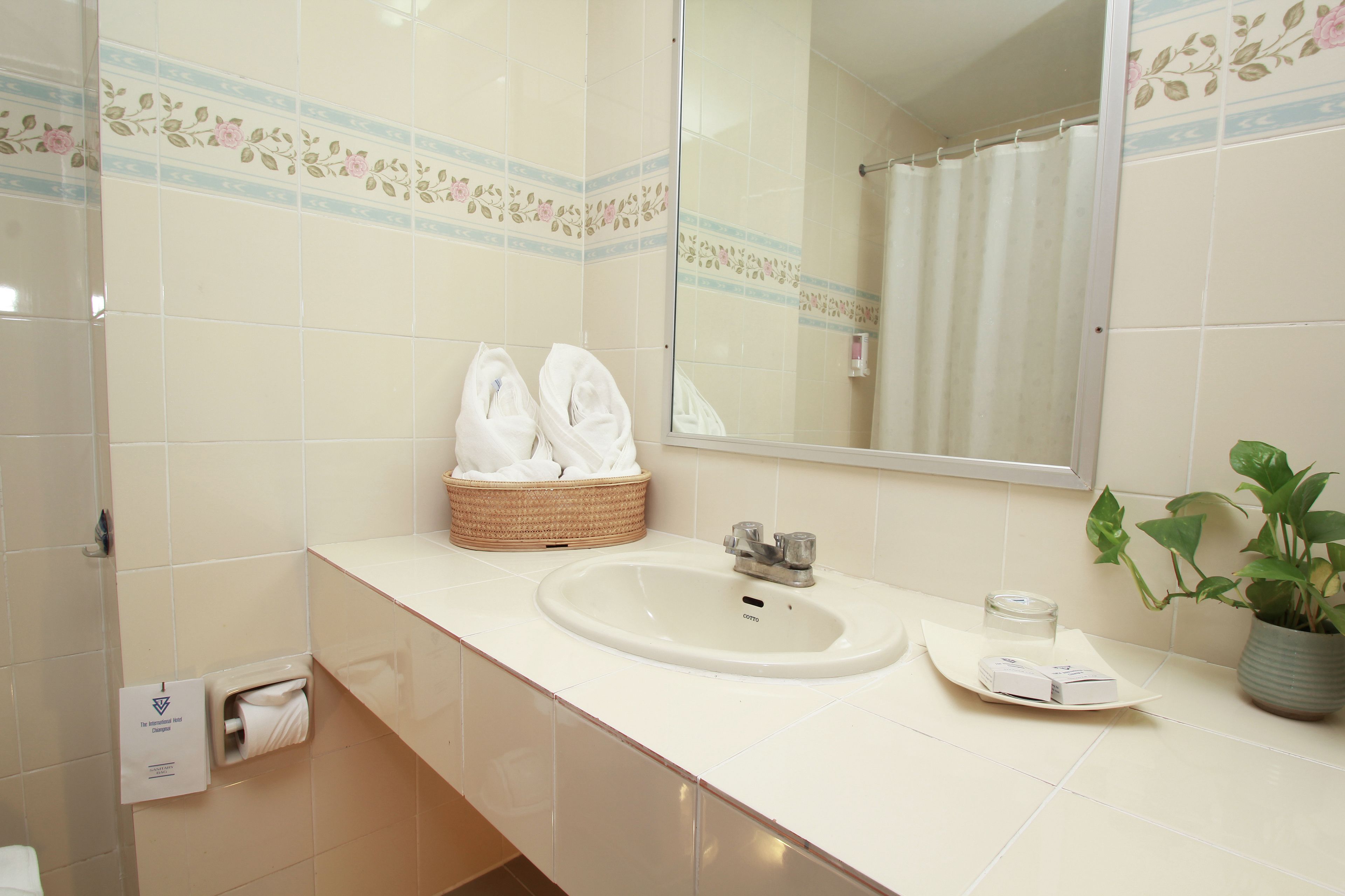 A bathroom with a sink, a mirror, a towel rack with towels, a basket, and a potted plant.