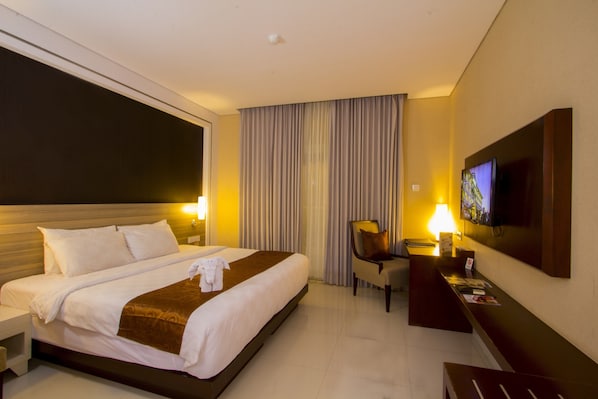 Habitación de hotel con una cama grande, un escritorio, una silla, un televisor y una ventana con cortinas.