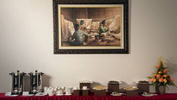 A dining table with a red tablecloth, coffee pots, plates, bowls, and a floral arrangement.