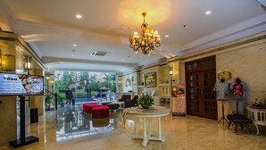 A spacious lobby with a chandelier, a reception desk, a red sofa, and a view of the outdoors. - Gallery Prawirotaman Hotel (Yogyakarta)