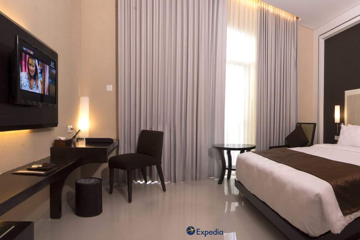 Een moderne hotelkamer met een groot bed, een bureau, een stoel, een klein tafeltje en een aan de muur bevestigde televisie.
