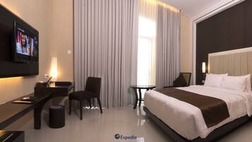 A modern hotel room with a large bed, a desk, a chair, a small table, and a TV mounted on the wall.