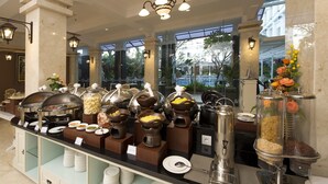 A buffet setup with various food stations, including pasta, meats, and grains, in a well-lit indoor area with large windows and decorative lighting. - Gallery Prawirotaman Hotel (Yogyakarta)