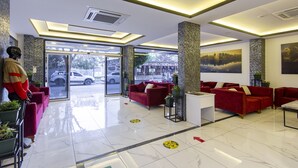 A modern lobby with red sofas, a mannequin, and a large window overlooking a parking area. - Aslan City Hotel (Alanya)