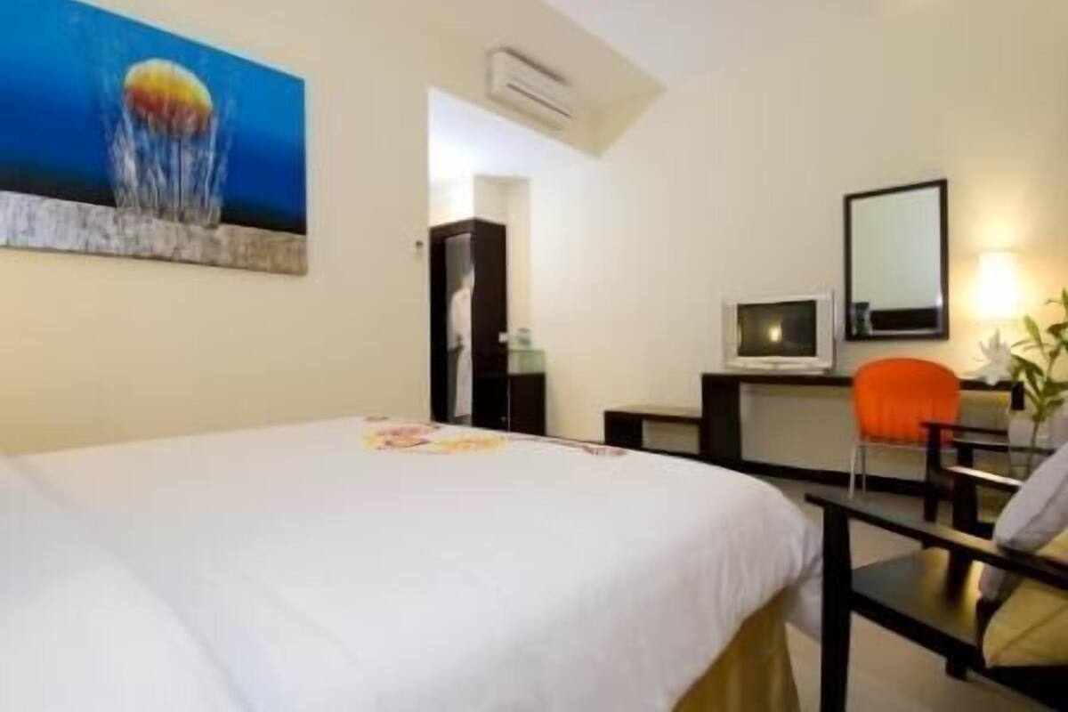 Hotellihuone, jossa on sänky, työpöytä, tuoli, televisio ja taulu seinällä.