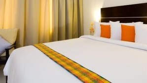 A hotel room with a large bed, white bedding, and orange pillows. - iShine Hotel (Pekanbaru)