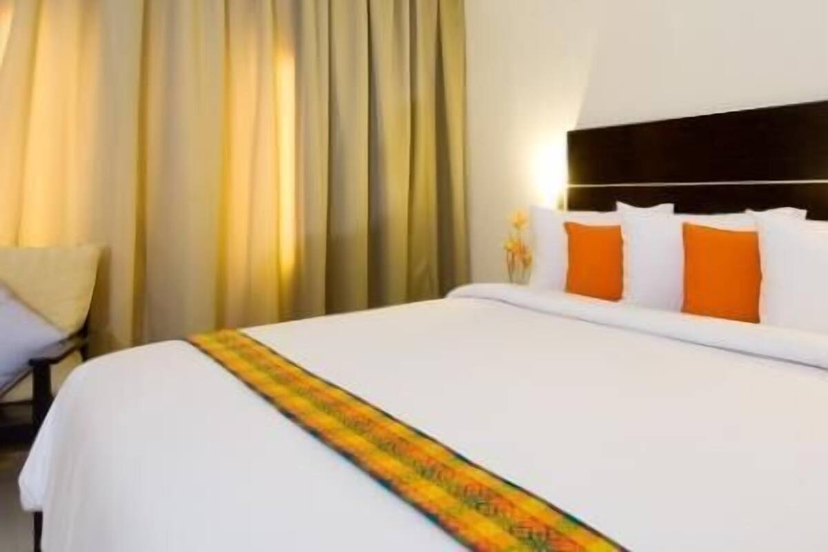 Hotellihuone, jossa on suuri sänky, valkoiset vuodevaatteet ja oranssit tyynyt.
