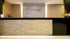 A reception desk with a modern design, featuring a textured wall and a sign that reads "iShine hotel". - iShine Hotel (Pekanbaru)