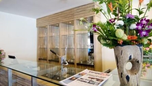 A modern interior with a glass table displaying a magazine, a wooden sculpture, and a vase with flowers. - iShine Hotel (Pekanbaru)