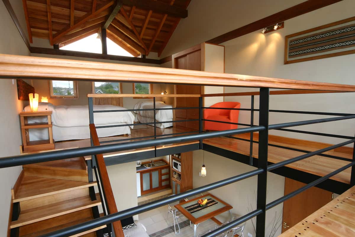 Habitación con varios niveles, una escalera de madera, una cama, una silla roja y una zona de comedor con mesa y sillas.