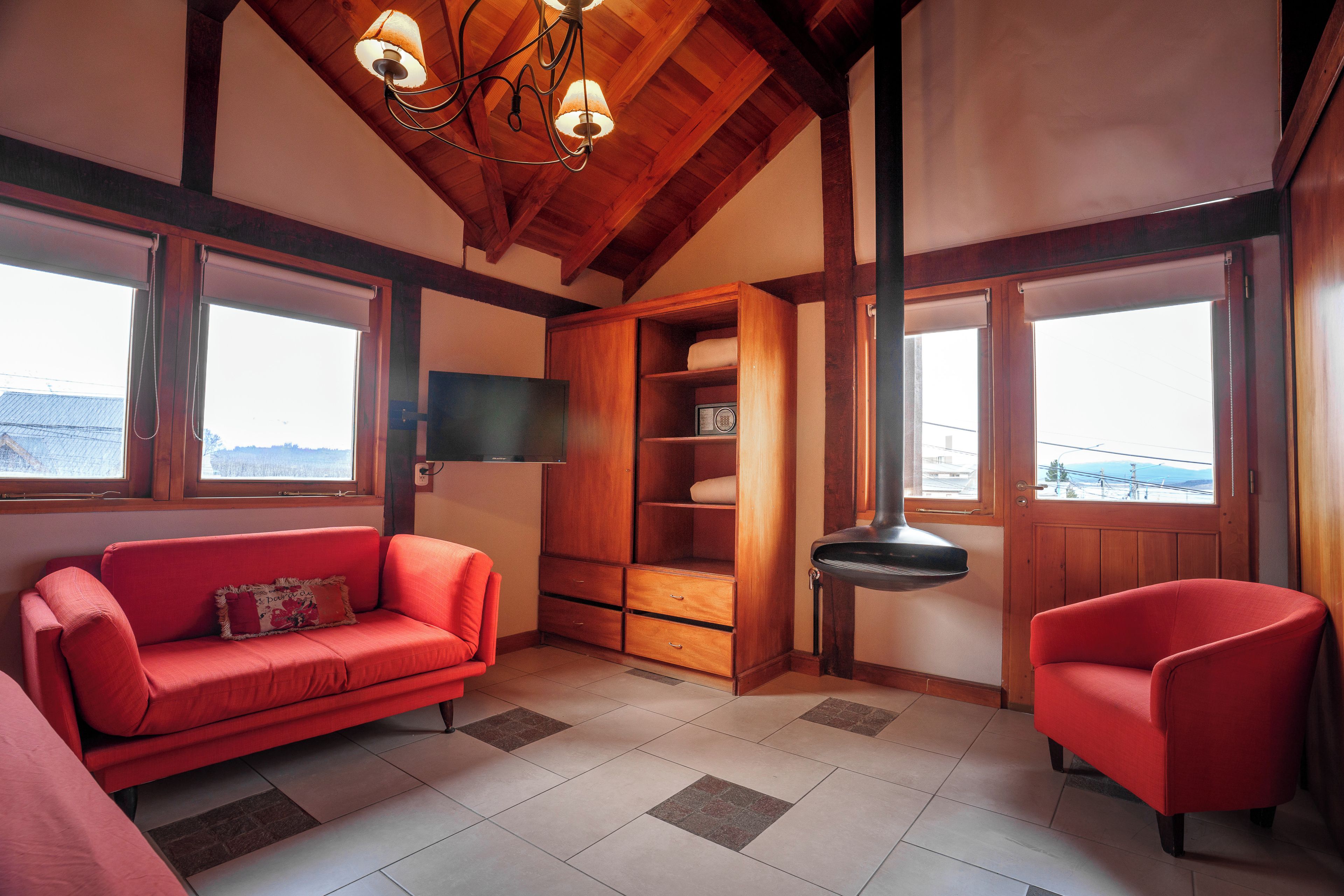 Quarto com sofá vermelho, armário de madeira, televisão e uma janela grande.