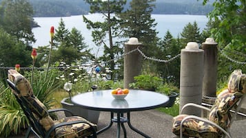A round table with chairs, a bowl of fruit, and a view of a lake and forest.
