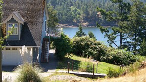 Una casa con balcón que da a un lago, rodeada de colinas boscosas.