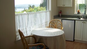 Una cocina pequeña con una mesa y sillas, una ventana que da a zonas verdes y un armario blanco.
