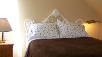 A bedroom with a white ornate headboard, lavender-patterned pillows, a brown bedspread, and a bedside lamp.