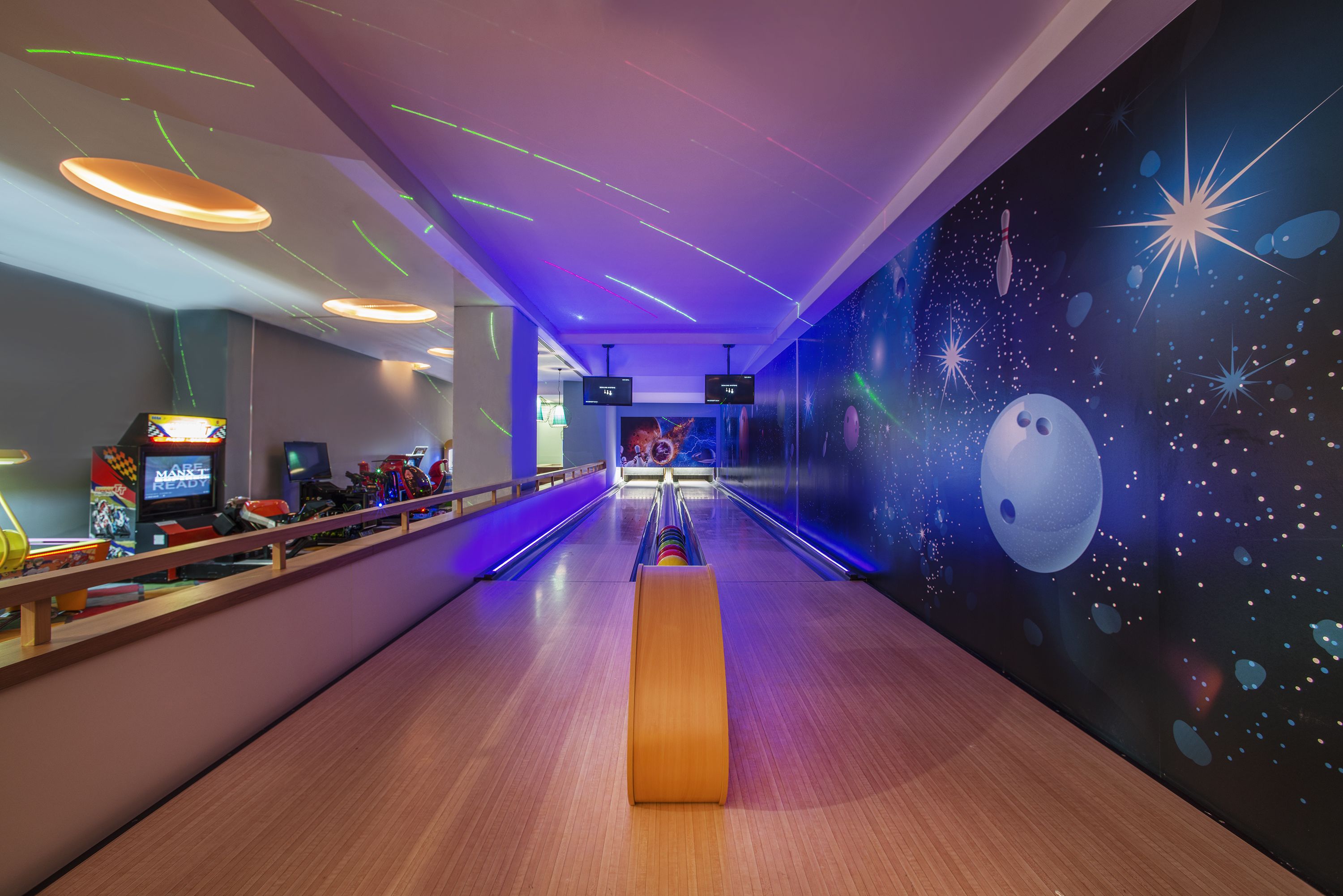 Een bowlingbaan met een houten vloer, neonverlichting en een muurschildering met een ruimtetema.