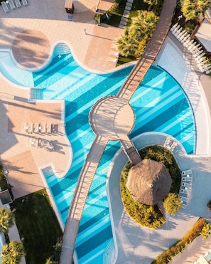 An aerial view of a swimming pool with a unique wavy design, surrounded by lounge chairs and a thatched umbrella. - Aska Lara Resort & Spa - All Inclusive (Antalya)