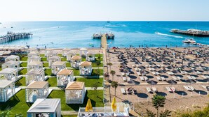 Un resort en la playa con varias cabañas tipo bungalow, un muelle y una zona de arena con sombrillas y sillas de sol.
