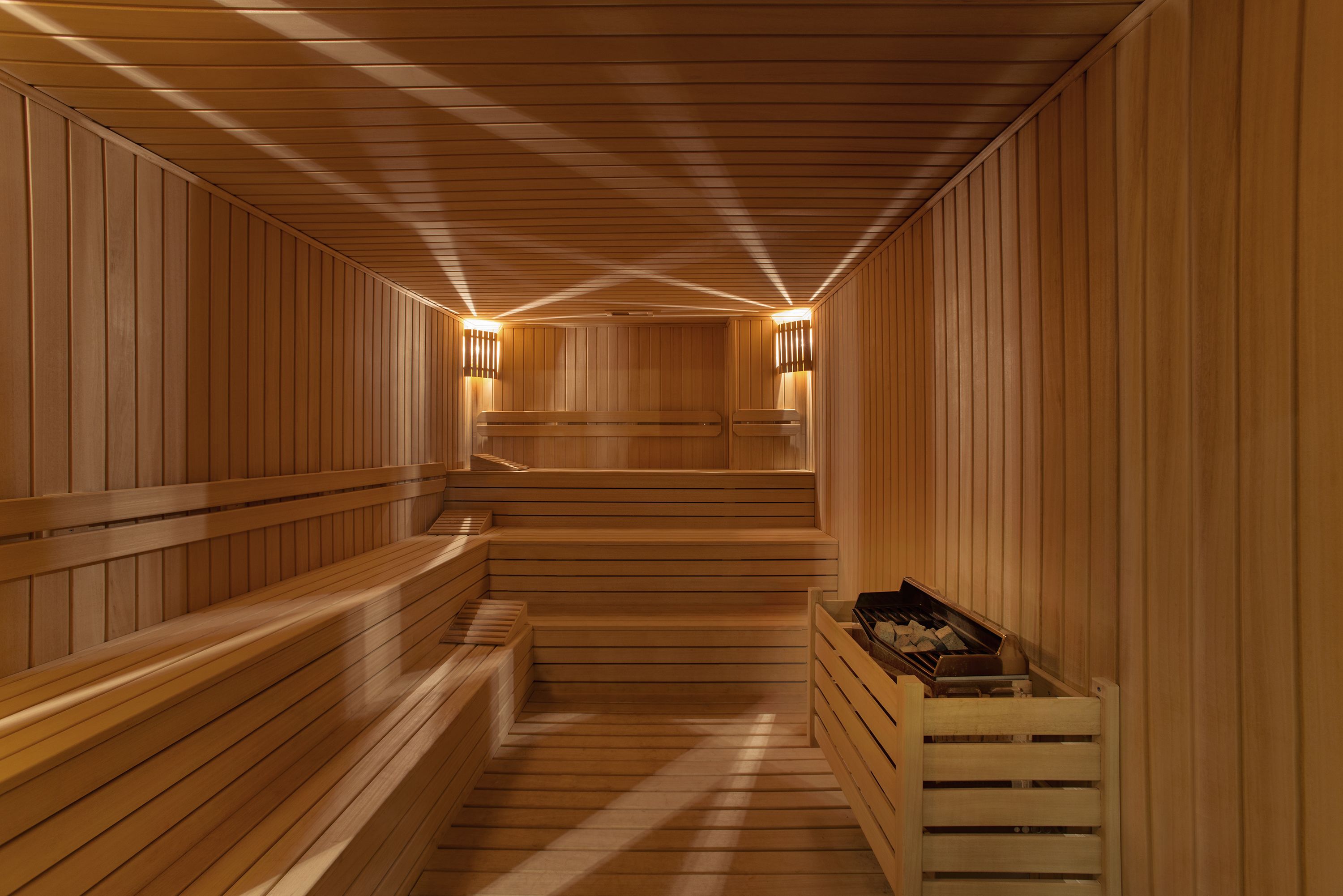A sauna with wooden benches and walls, and two wall-mounted light fixtures.