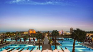 Zona de piscina en un resort con varias piscinas, palmeras y una vista distante del océano.