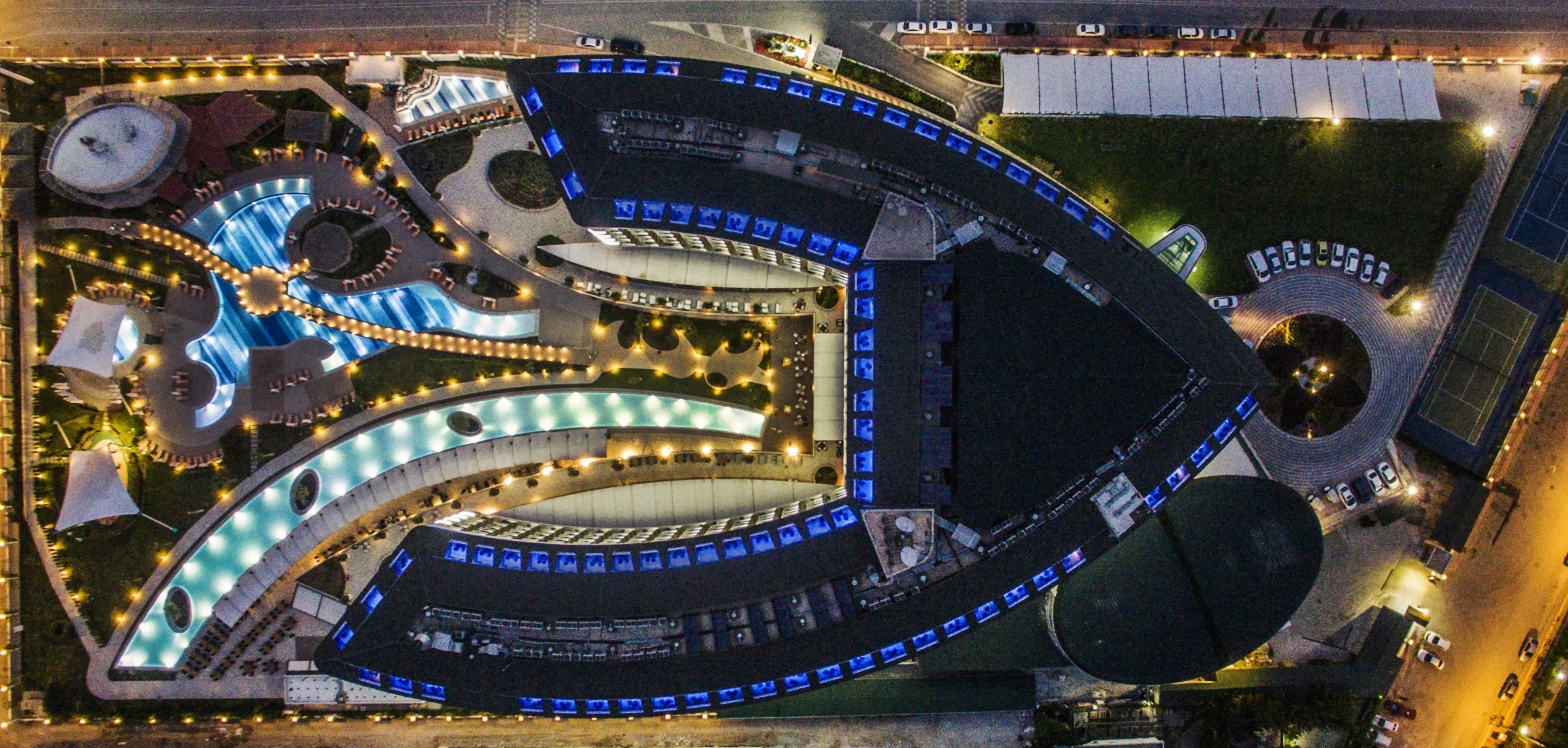 An aerial view of a complex with multiple interconnected buildings, featuring a central circular structure, various pathways, and landscaped areas.