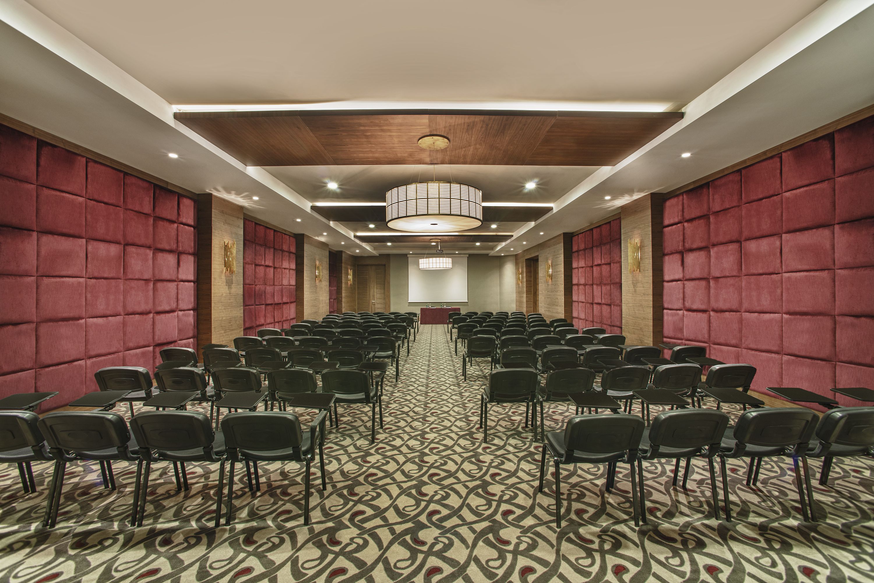 A conference room with rows of chairs, a patterned carpet, and a wooden ceiling.
