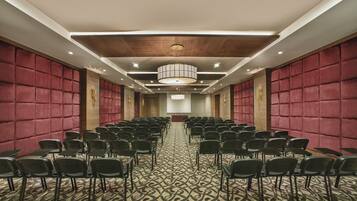 A conference room with rows of chairs, a patterned carpet, and a wooden ceiling.