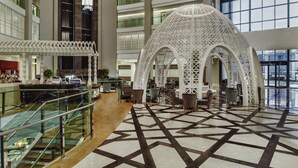 Un lobby moderno de hotel con un suelo de baldosas geométricas, un área de estar central y una estructura blanca decorativa.