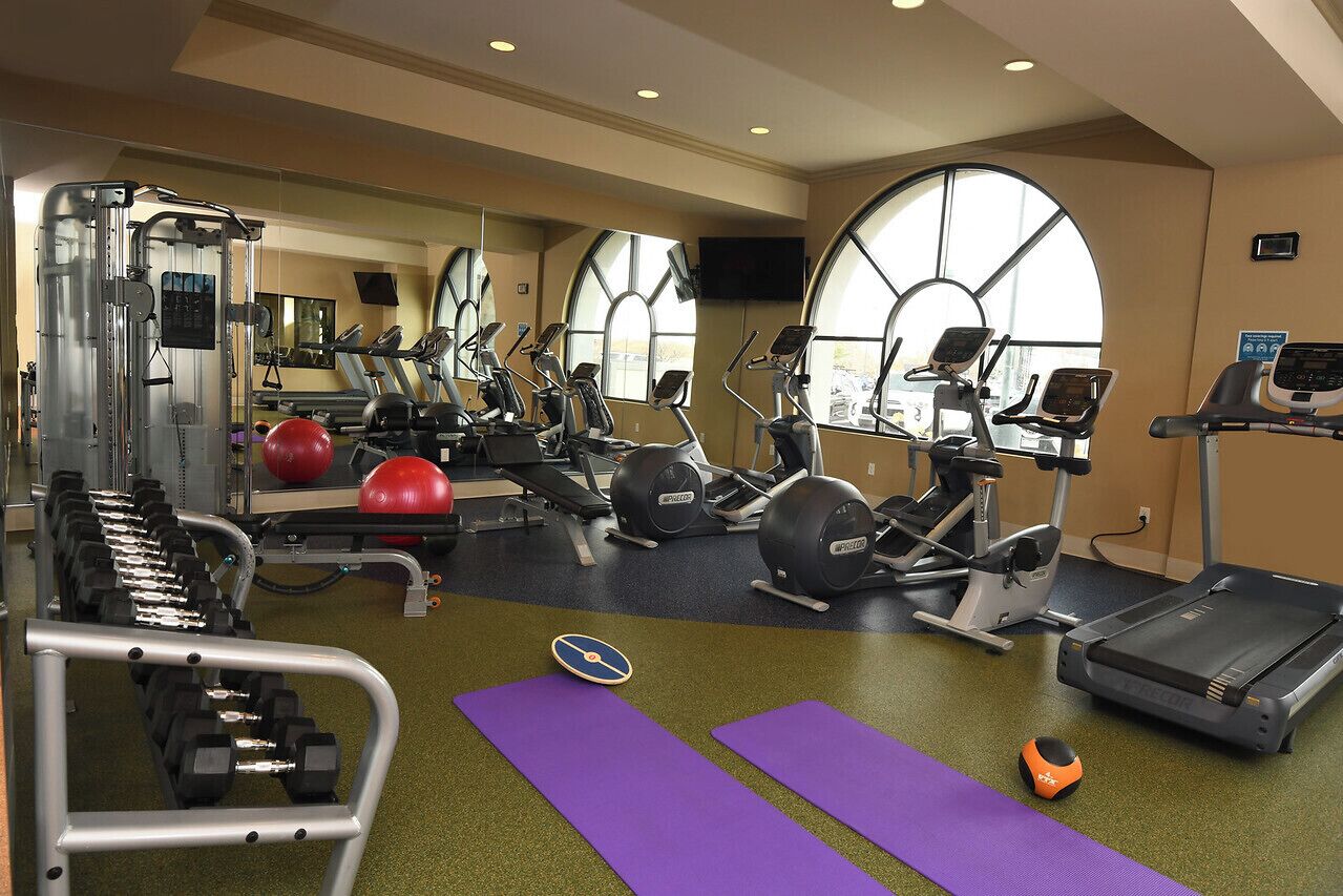 A gym with exercise equipment, mirrors, and large windows.